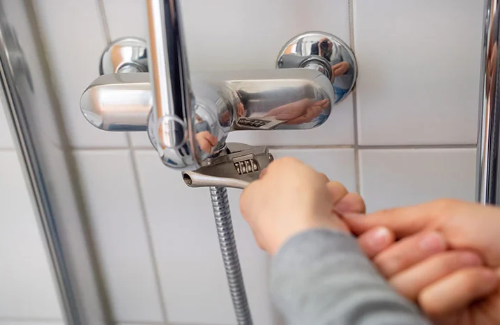 Person montiert Duschschlauch mit Rohrzange.